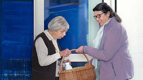 Frau bringt Seniorin Essenskorb