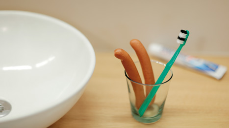 Un paio di salsicce in un barattolo accanto a uno spazzolino da denti verde.