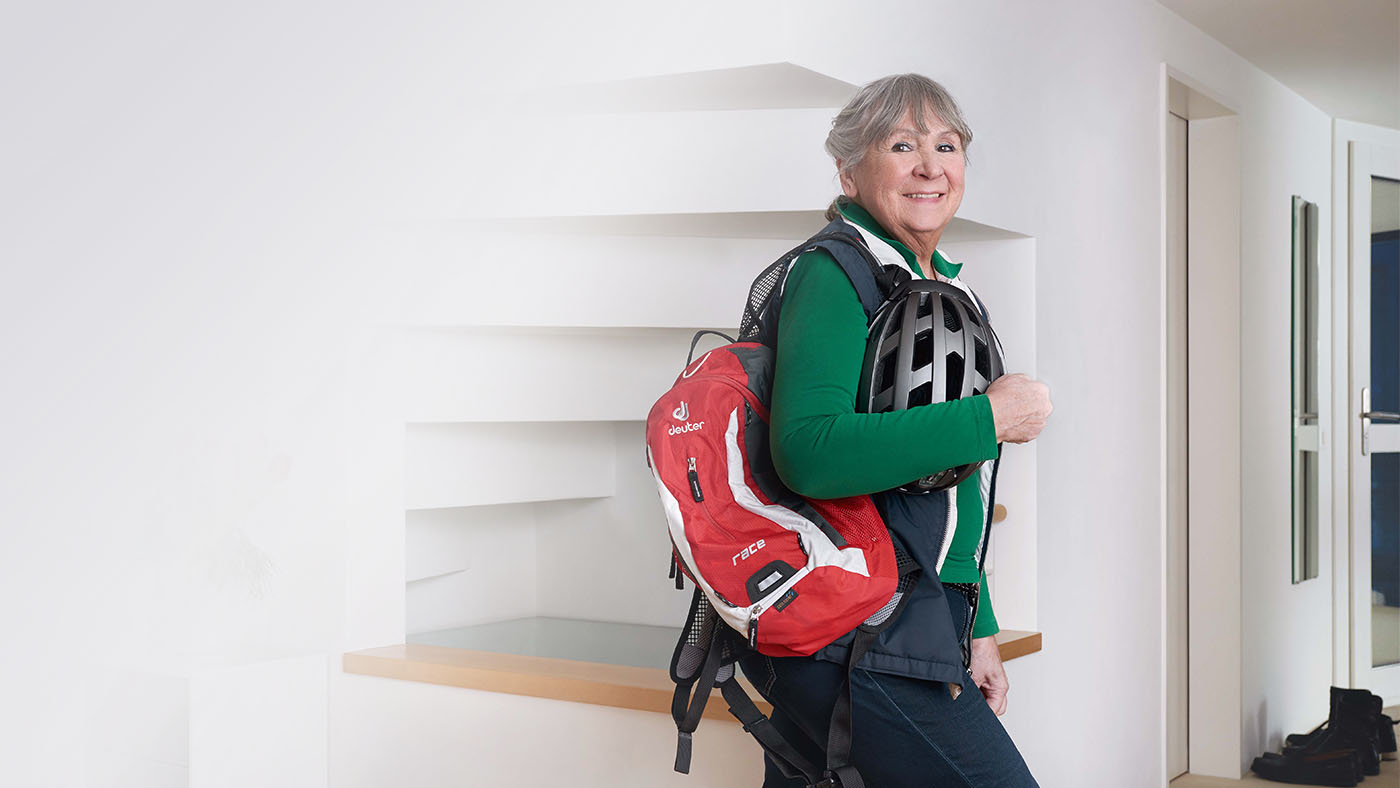 Frau mit Sporttasche und Velohelm geht aus dem Haus